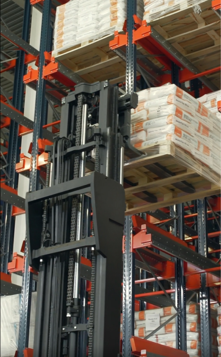 Вилочный погрузчик поднимает паллет с мешками в высоком складском стеллаже с оранжевыми элементами крепления, взгляд снизу вверх