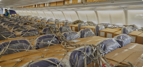 Внутри самолета, заполненного коробками, сотрудники упаковывают груз. Стулья накрыты пленкой, а коробки надежно зафиксированы.